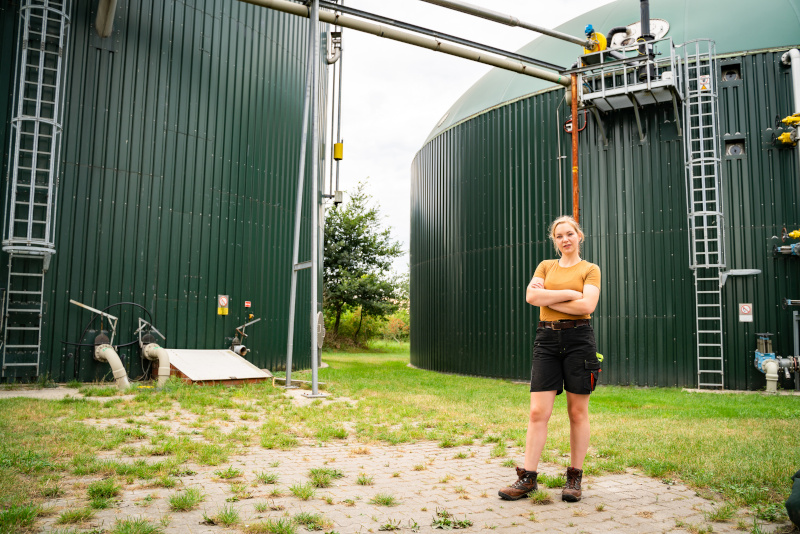Betrieb einer modernen Biogasanlage zur Stromerzeugung - junge Landwirtin vor einem Fermenterbehälter. Landwirtschaftliches Symbolfoto.